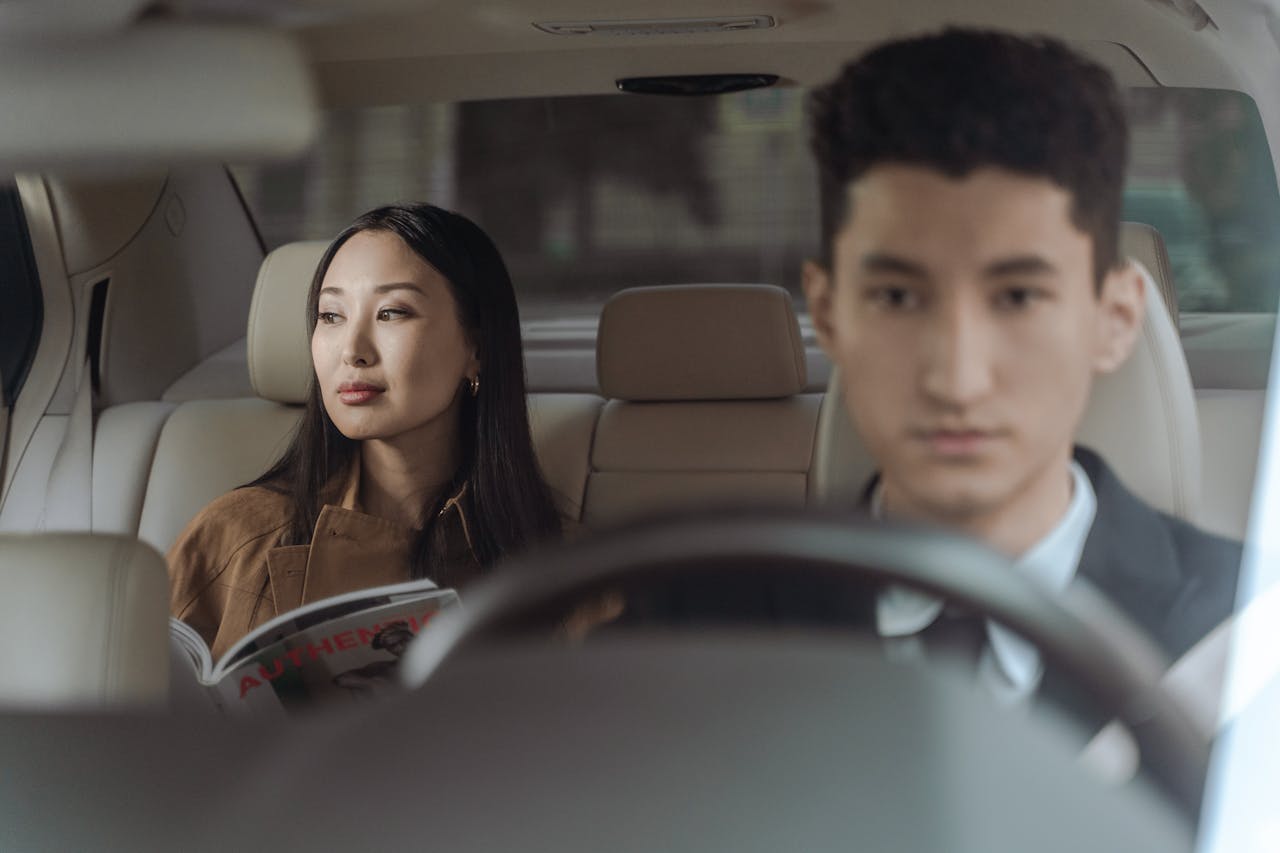 Asian businesswoman and male chauffeur in a luxury car interior, representing travel comfort and professional transportation.